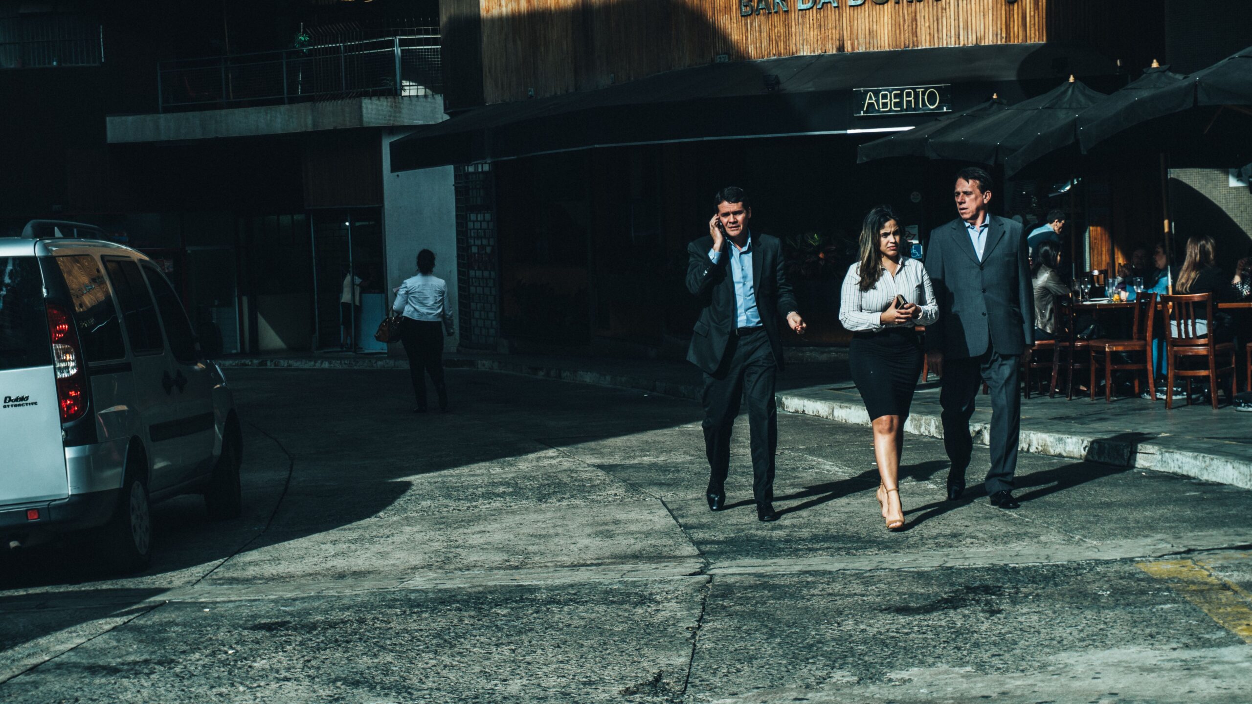 Three business professionals walk along a city street outside a cafe.